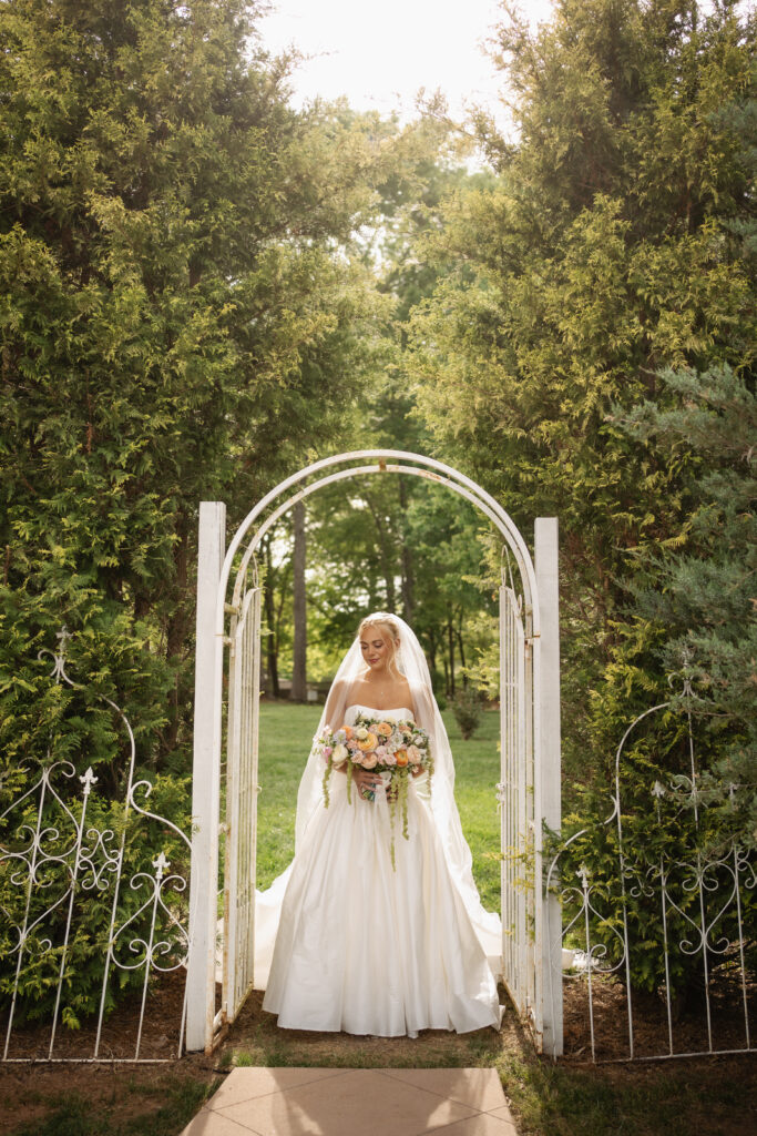 Bridal portrait before wedding featuring bride beneath garden arch in elegant outdoor wedding setting.